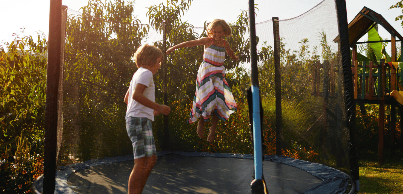 Two kids jumping on a large trampoline outdoors.