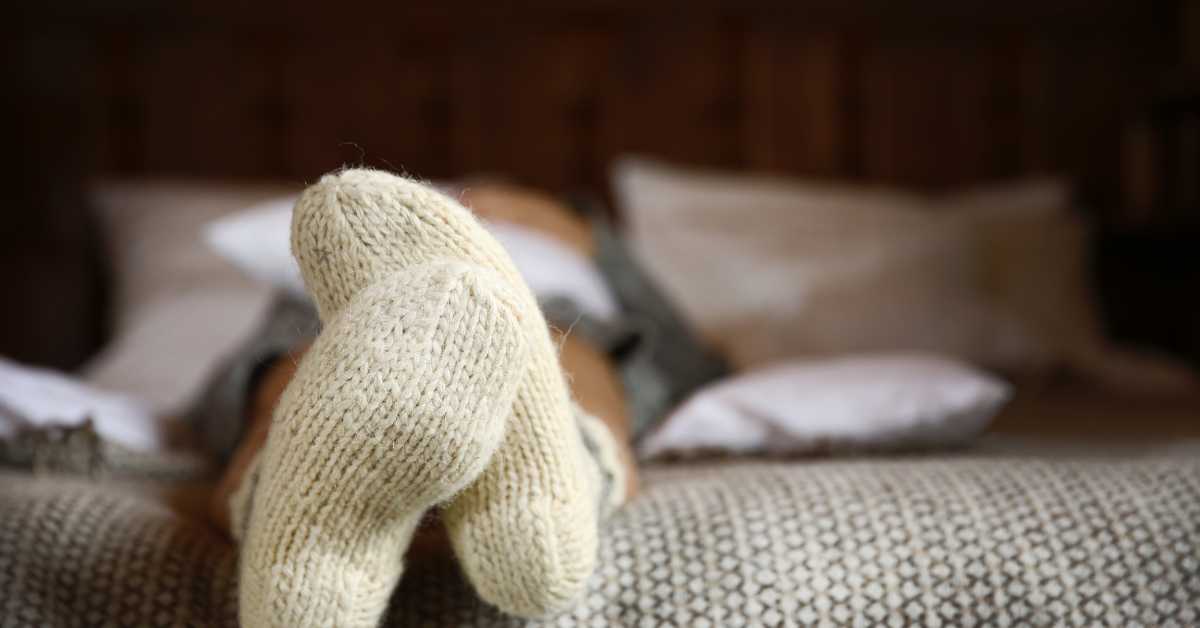 A person lays on a bed with wool socks on their feet.