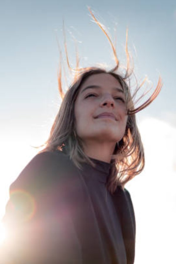 A young woman smiling and enjoying the breeze and sunset from a mountain viewpoint.