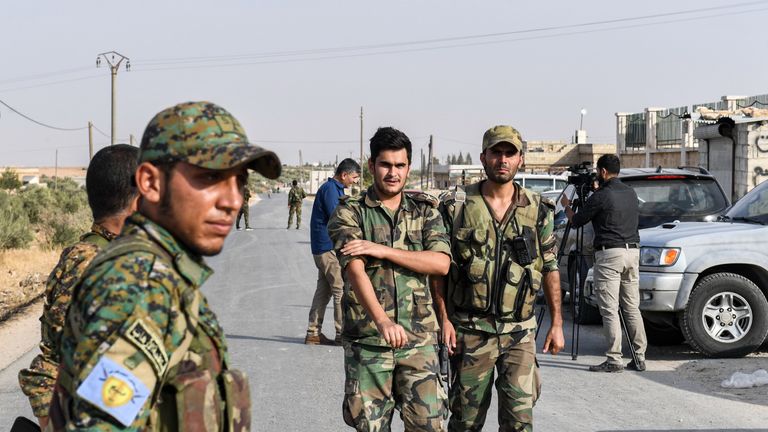 A fighter (L) wearing a military uniform bearing the insignia of the Manbij Military Council (MMC), affiliated with the Syrian Democratic Forces (SDF) Kurdish-led alliance, stands by as Syrian government soldiers walk past at a position on the outskirts of the northern city of Manbij in the north of Aleppo province, as government forces deploy there on October 15, 2019. (Photo by - / AFP) (Photo by -/AFP via Getty Images)
