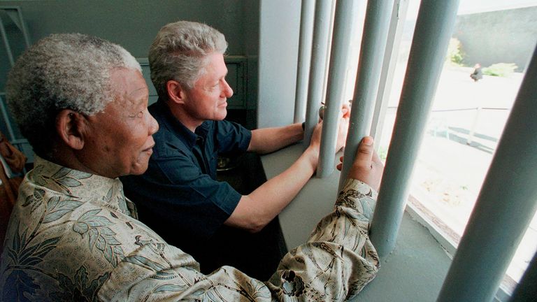 FILE -  Nelson Mandela, left, and former US president Bill Clinton look to the outside from Mandela's Robben Island prison cell in Cape Town, South Africa March 27, 1998. The Mandela Foundation has strongly condemned the auction of the key to Mandela's  prison cell which is set to go under the hammer next month. (AP Photo/Scott Applewhite, Pool, File)