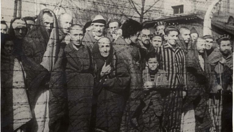 Holocaust survivors stand behind a barbed wire fence after the liberation of Nazi German death camp Auschwitz-Birkenau in 1945. Pic: Yad Vashem Archives/Handout via Reuters