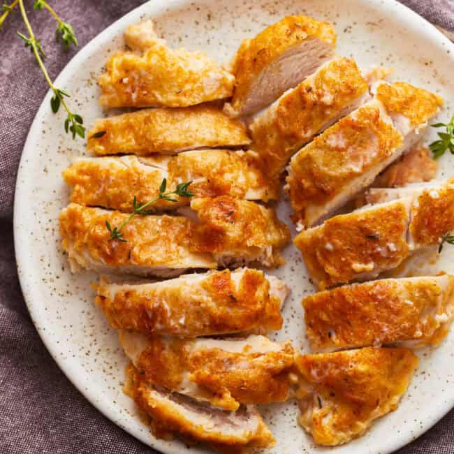 overhead view of 2 sliced butter baked chicken breasts on a white plate.