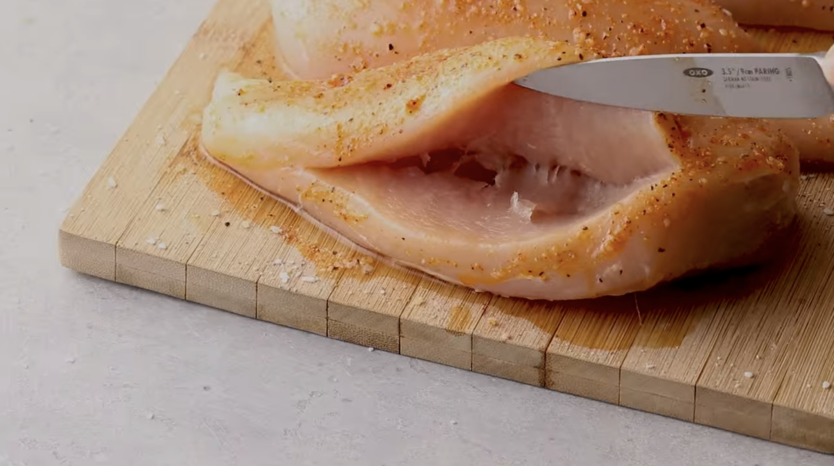 Paring knife cutting into the side of a chicken breast to create a pocket.