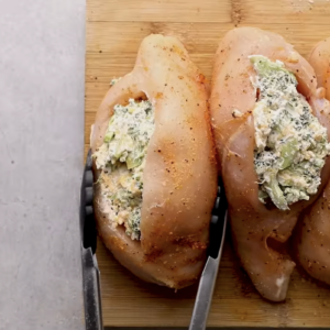 Raw stuffed chicken breasts are on a cutting board.