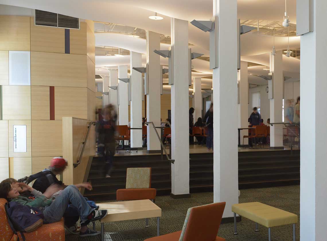 Students seated and walking in an interior hallway and lounge with colorful wall accents and furniture