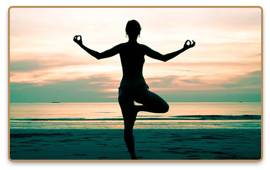 Woman practices metitation on the beach in a tree yoga pose