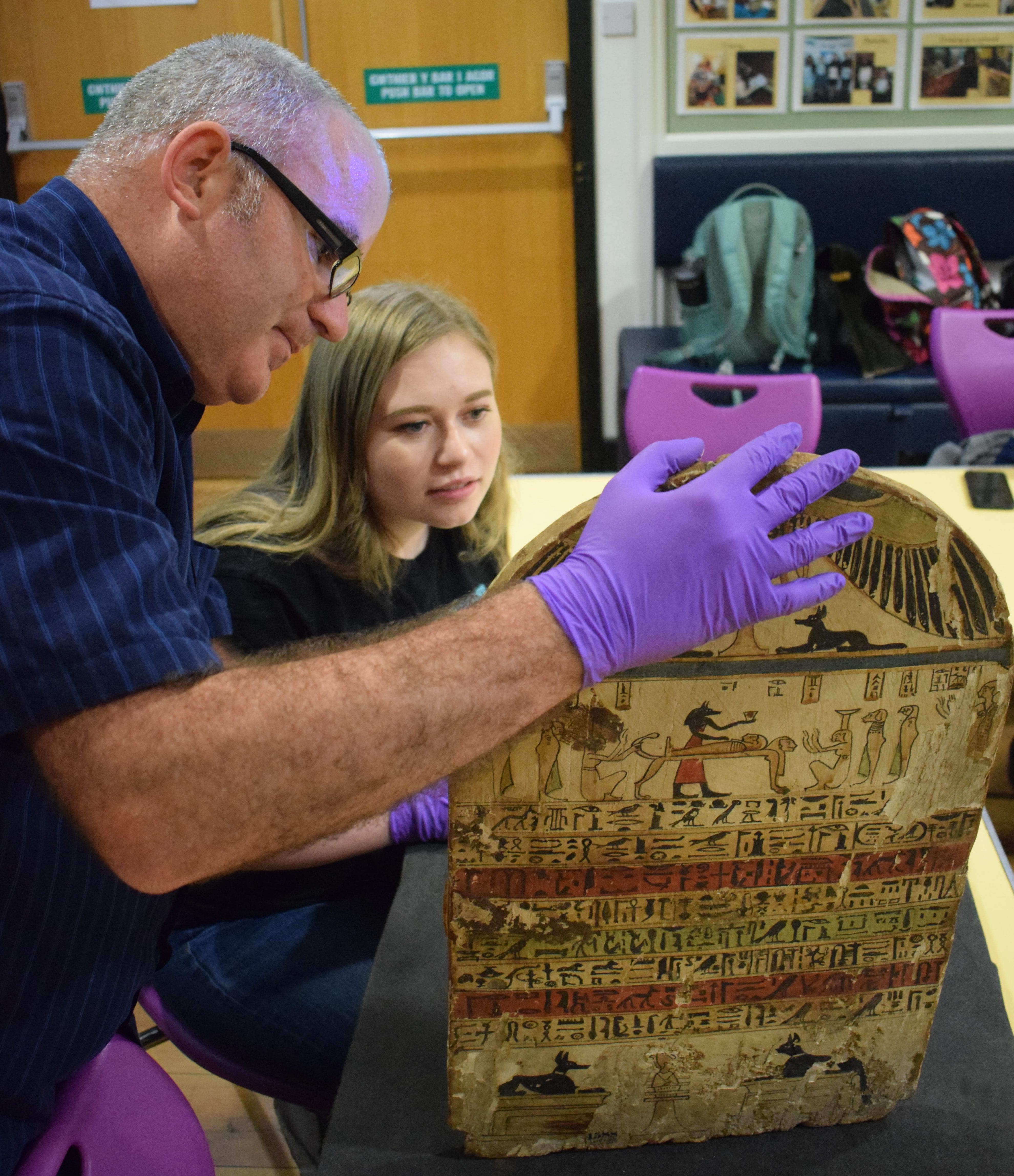 Photo of a man (Ken Griffin) holding a colourful stela while a young female student looks at the back of it. 