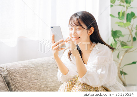 Woman sitting on a sofa and looking at a smartphone 85150534