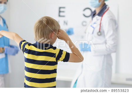 Boy on appointment in clinic, oculist cabinet, sight diagnostic closing eye and say out loud letter on board 89553823