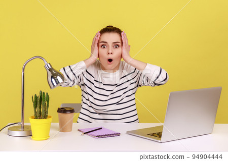 Amazed shocked woman office manager looking at camera with big eyes and open mouth, keeps hands on head, having problems with her work. Indoor studio studio shot isolated on yellow background. 94904444