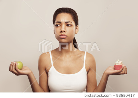 Lovely african american woman makes a choice between cake and apple on white 98680417