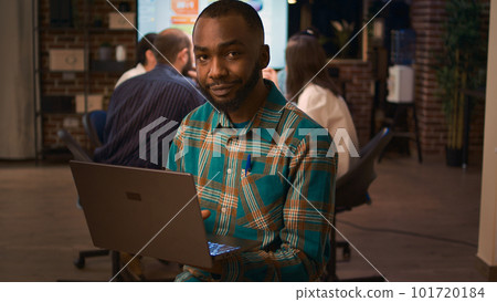 African american office employee working on laptop portrait, front view. Smiling man holding computer, looking at camera medium shot, company financial presentation, business meeting 101720184