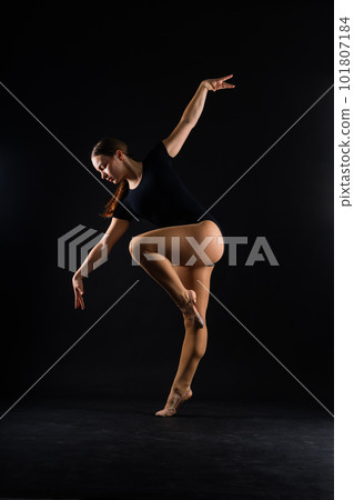 A girl gymnast in a swimsuit does tricks on a white and dark background. Front view 101807184