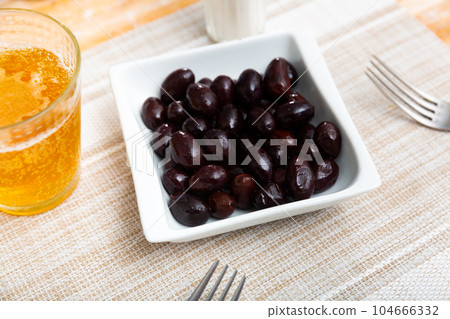 On square white plate lies portion of large ripe black olives with stone. 104666332