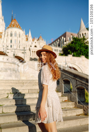 Happy young woman in hat at dawn enjoys view of beautiful buildings. Lifestyle, recreation concept. 105108166