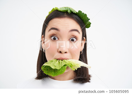 Close up portrait of smiling asian woman eating lettuce, loves cabbage, vegetarian enjoys raw organic food, white background 105605095