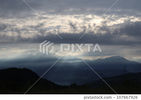 A morning landscape where you can see a sea of clouds and mountains, with crepuscular rays extending through the gap in the sky covered with clouds. 107667926