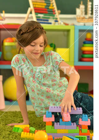 Portrait of cute girl playing with colorful plastic blocks in room 107928611