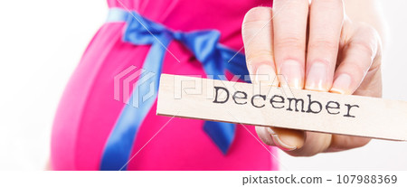 Pregnant woman in pink dress with blue ribbon showing word december 107988369