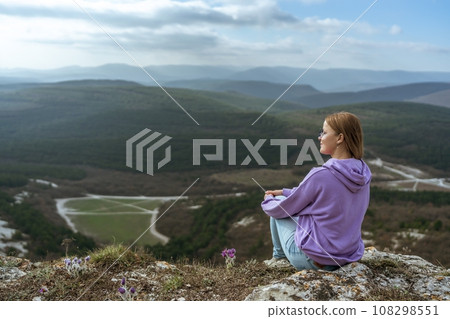 Girl on mountain peak looking at beautiful mountain valley in fog at sunset in summer. Landscape with sporty young woman, foggy hills, forest, sky. Travel and tourism, hiking 108298551