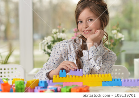 Portrait of cute girl playing with colorful plastic blocks in room 109139701