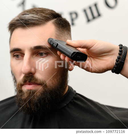 Barber shaves the temple with cordless trimmer during a short haircut on the sides of the head. 109772116