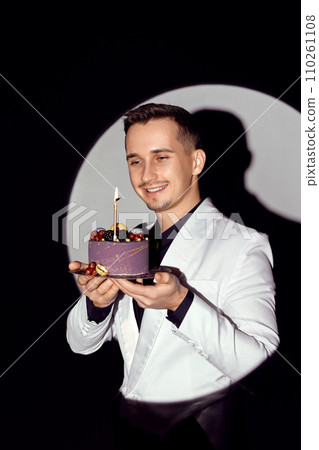 elegant caucasian man in white suit tuxedo holding cake with candle in the circle of light, 110261108