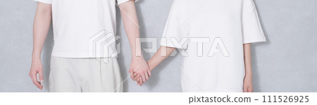 A smiling couple holding hands in front of a wall and cuddling together in linked coordination 111526925