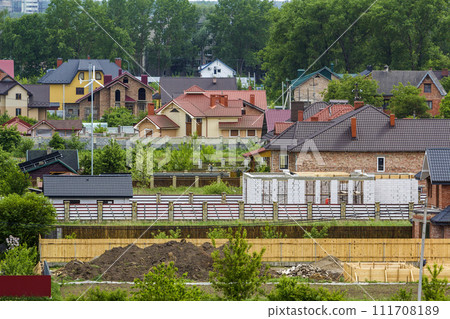 Beautiful view summer panorama of modern quiet suburban residential area. Nice comfortable two- storied new cottages with colorful tile roofs, yards and gardens on distant high buildings background. 111708189