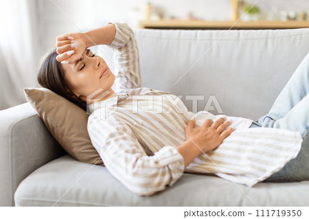 Sick young woman lying on couch, feeling unwell at home 111719350