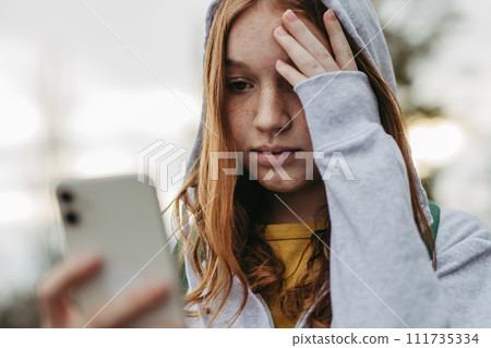 Portrait of teenage girl looking at her smartphone, sad, anxious, alone. Cyberbullying, girl is harassed, threated online. 111735334