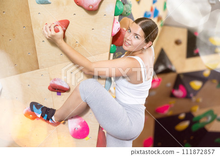 Young Europian woman climbs steep artificial wall in sports complex and trains endurance 111872857