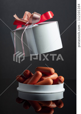 Opened gift box with sausages on a black background. 112101164