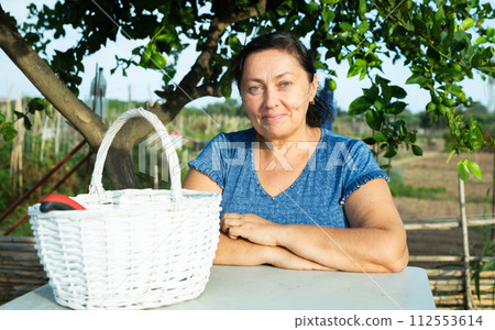 Happy elderly woman sitting at table under green tree in home garden 112553614