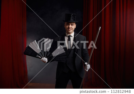 Magician performing miracle trick on stage using fan and cane 112812948