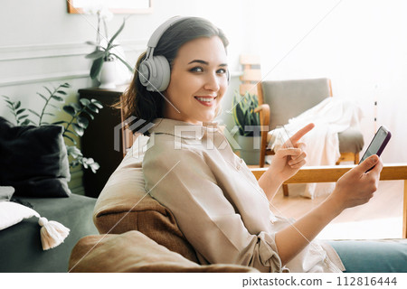 Happy Young Woman with Wireless Headphones Smiles, Points to Smartphone, Reading a Message. Joyful 112816444