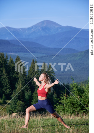 Woman doing morning exersices in mountains. Attractive young female enjoying freedom, outdoors. Flexible woman stretching, breezing with closed eyes, admiring landscape. Concept of freedom. 113623918