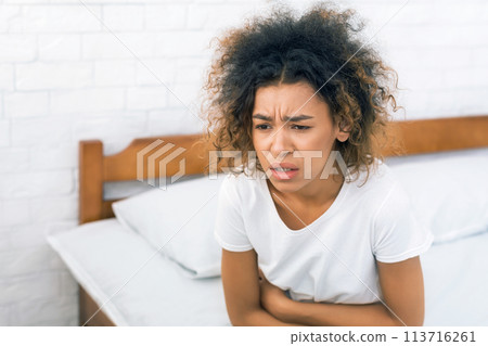 African-american woman having painful stomachache, sitting on bed 113716261