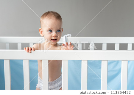 Interested baby leaning on the back of a wooden crib 113864432