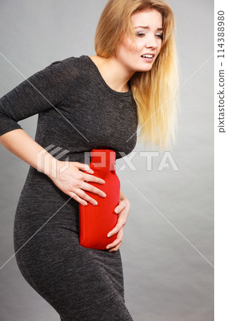 Girl having stomach ache, holding hot water bottle 114388980