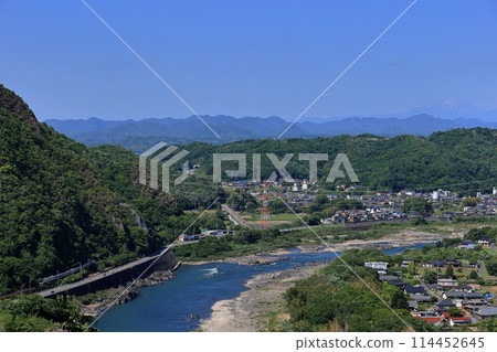 The Hida Express train runs along the Kiso River with Mount Ontake in the background and fresh greenery. 114452645