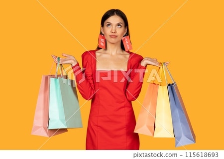 A woman dressed in a chic red dress stands against a warm yellow background, her hands holding several shopping bags in various pastel shades. Bright red sale tags are attached to her ears 115618693