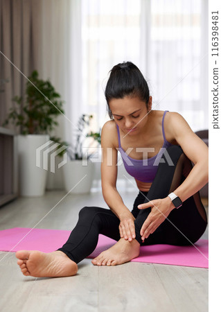 sad woman sitting on yoga mat touching ankle that hurts, sport injury , woman feeling pain. 116398481