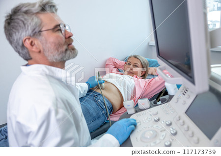 Gray-haired male doctor working with patient and making ultrasonography 117173739