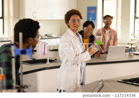 In high school laboratory, teacher demonstrating experiment with beaker to students 117214356