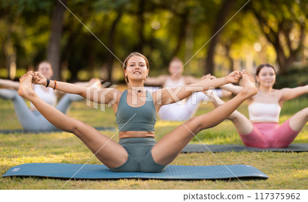 Girls practicing hatha yoga in summer garden, stretching in an asymmetrical seated asana Parivritta Janu Sirsasana with a forward bend and an outstretched arm 117375962