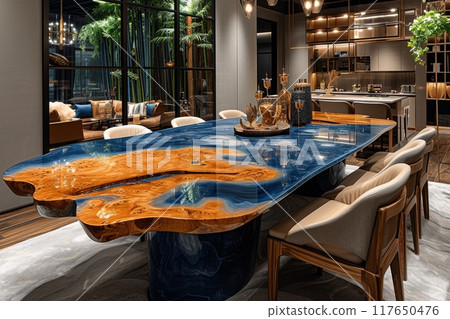 Large wooden dining table with a unique epoxy resin design, decorated in blue and brown tones, is surrounded by chairs. Dining room has a modern and refined atmosphere 117650476