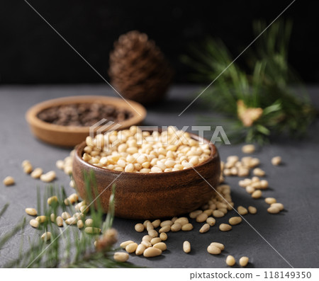 Pine nuts in a bowl and a handful of unpeeled nuts on a gray background with a branch 118149350