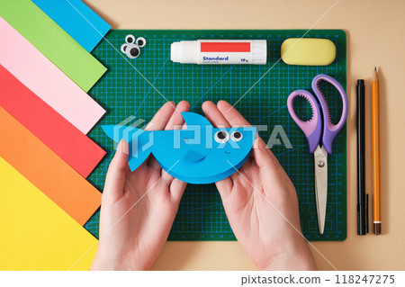 Women's hands hold a blue shark craft on a background of paper crafting tools. Idea for hobby and art 118247275